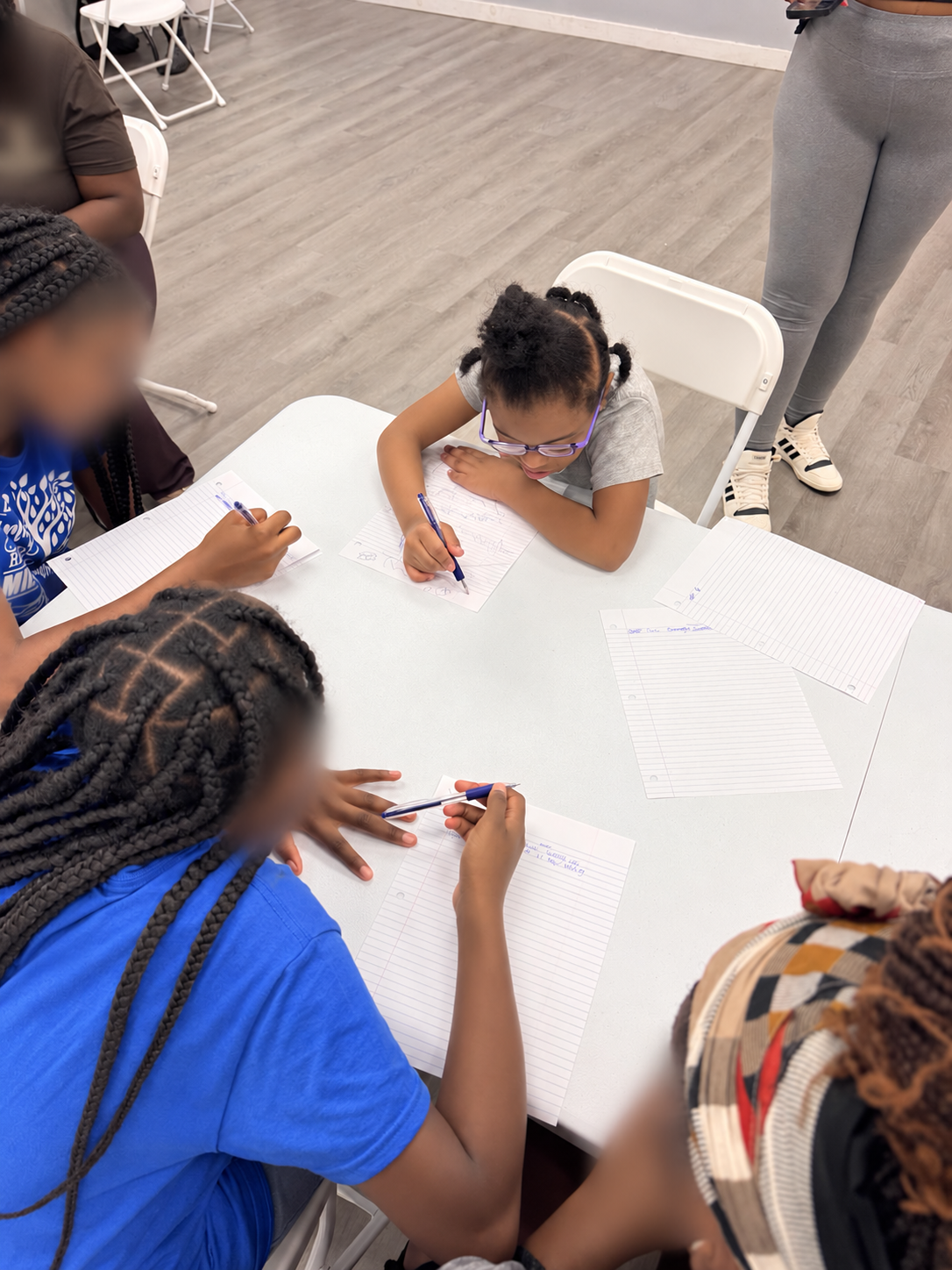 Young participants, including Roshelle's daughter, engaged in a guided journaling activity; other faces blurred for privacy