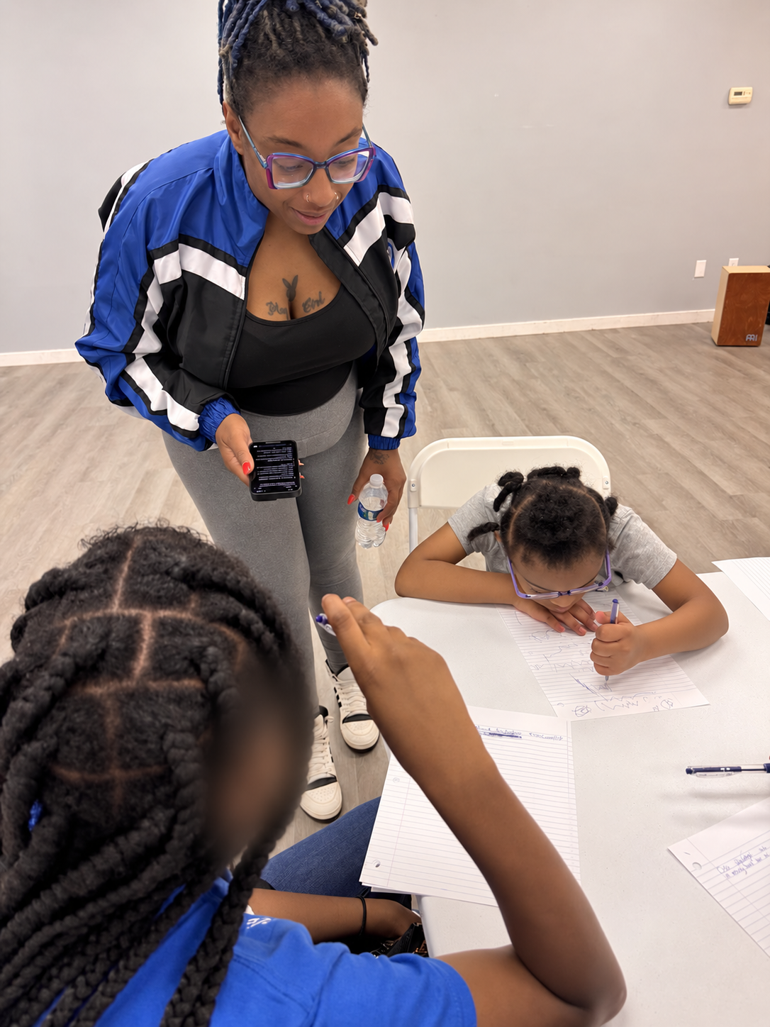 Roshelle guiding her daughter and another participant through a journaling activity; other participant blurred for privacy